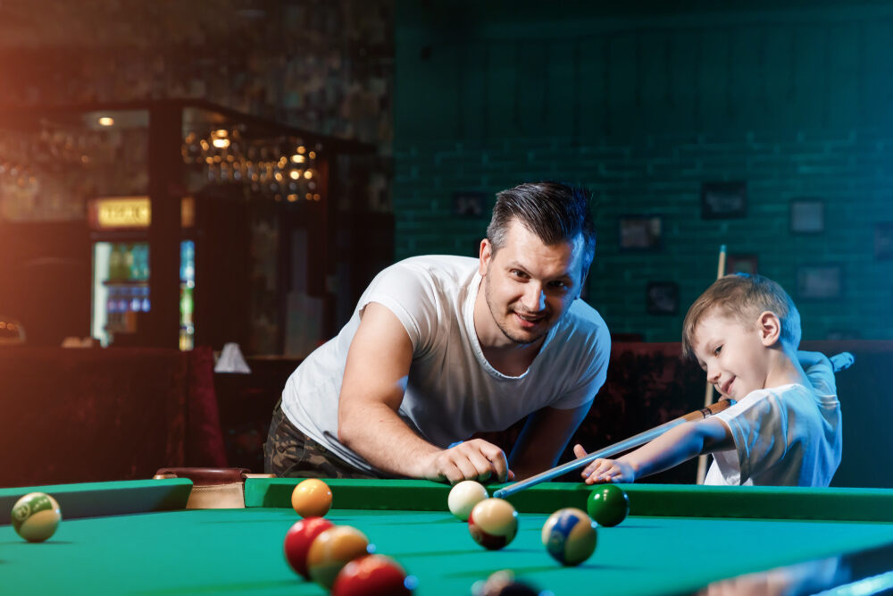 A father helps his son play pool.