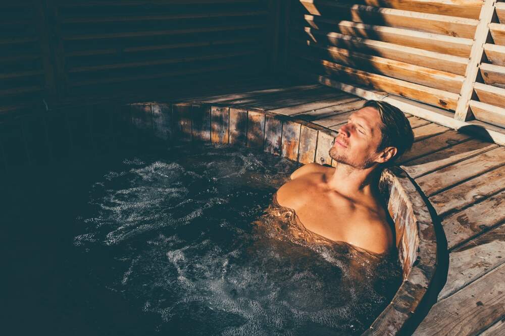 A blissful man relaxes with his eyes closed in a rustic outdoor hot tub